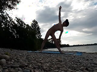 Slender nudist Jon Arteen practices yoga on a naturist beach, showcasing his flexibility and physique.